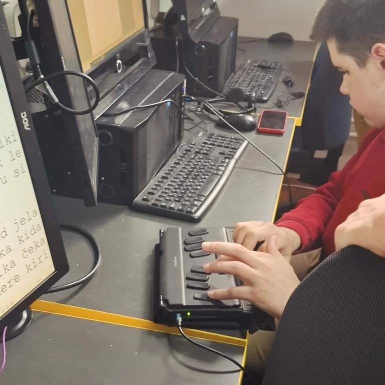 Korisnik Deni objašnjava gostima brajevu elektroničku bilježnicu koju koristi kao brajev redak